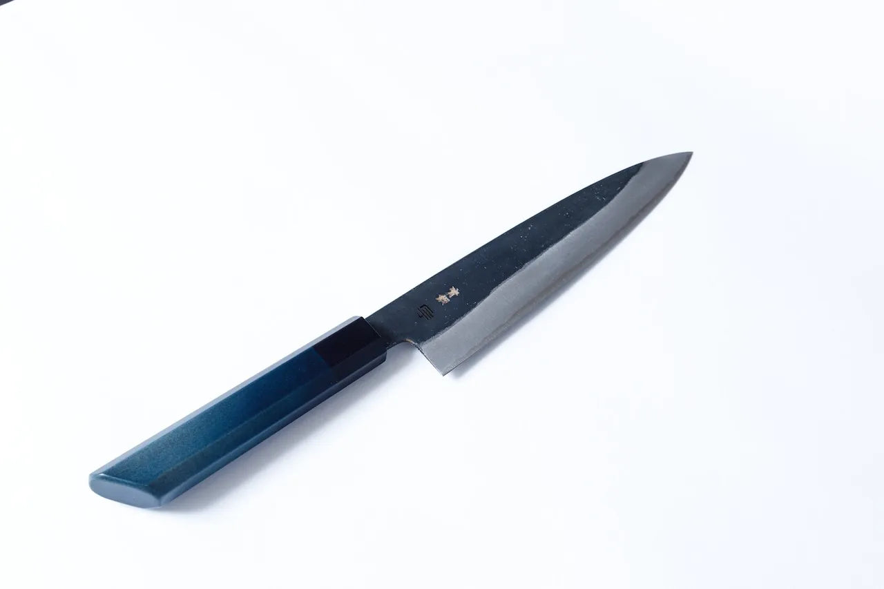 Cuchillo Gyuto artesanal de 210mm con hoja de acero al carbono forjado y mango teñido en añil, fabricado por maestros de Sakai y Tokushima.