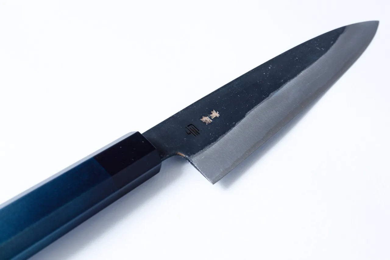Cuchillo Gyuto artesanal de 210mm con hoja de acero al carbono forjado y mango teñido en añil, fabricado por maestros de Sakai y Tokushima.